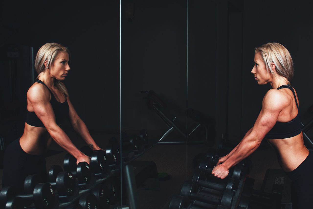 Deux athlètes enchaînent un mouvement d'haltères face au miroir d'une salle